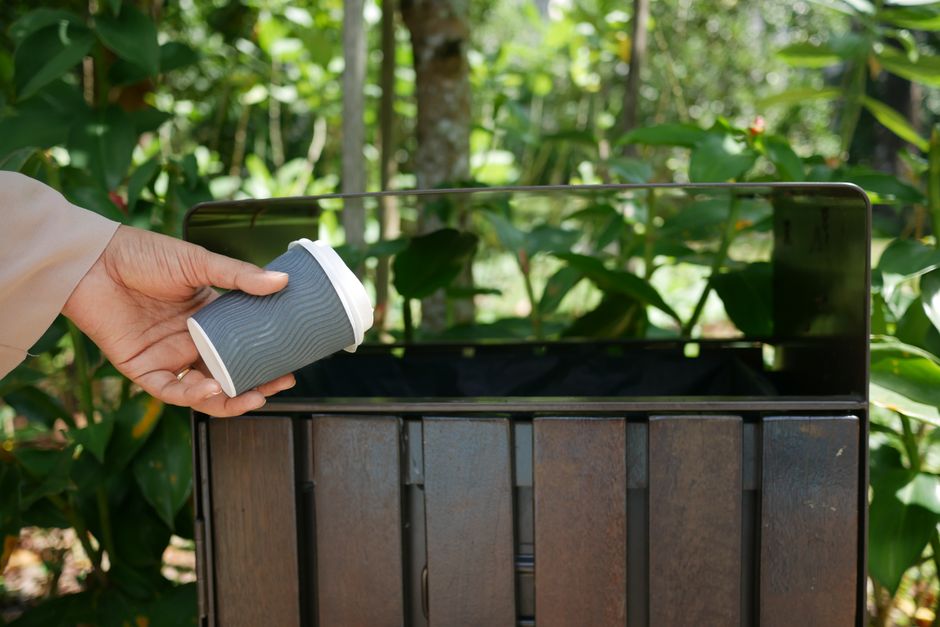 Outside a building with a grey concrete exterior wall and a metal door secured with a handle, a group of four blue plastic trash bags filled with waste are placed on the concrete pavement next to the